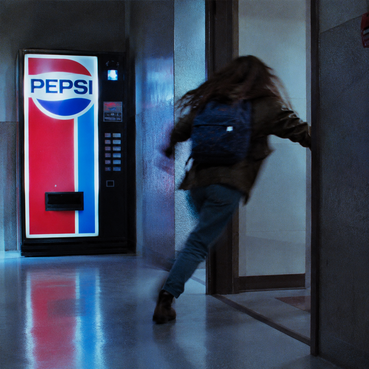 A cinematic shot from the movie "Terminator 2", shot from the side and from behind. A young 14-year-old Gabrielle, dressed in jeans, a jacket and boots, runs out of the doorway into the hallway in a panic. Her body is very blurred when moving, her waving arms and disheveled hair emphasize her extreme speed. She's wearing a blue backpack. To the left of the doorway, a brightly illuminated vintage red and blue Pepsi vending machine can be seen in the background. High contrast, cool aesthetics of a 1990s action movie, 35 mm film grain, photorealistic frame capture.